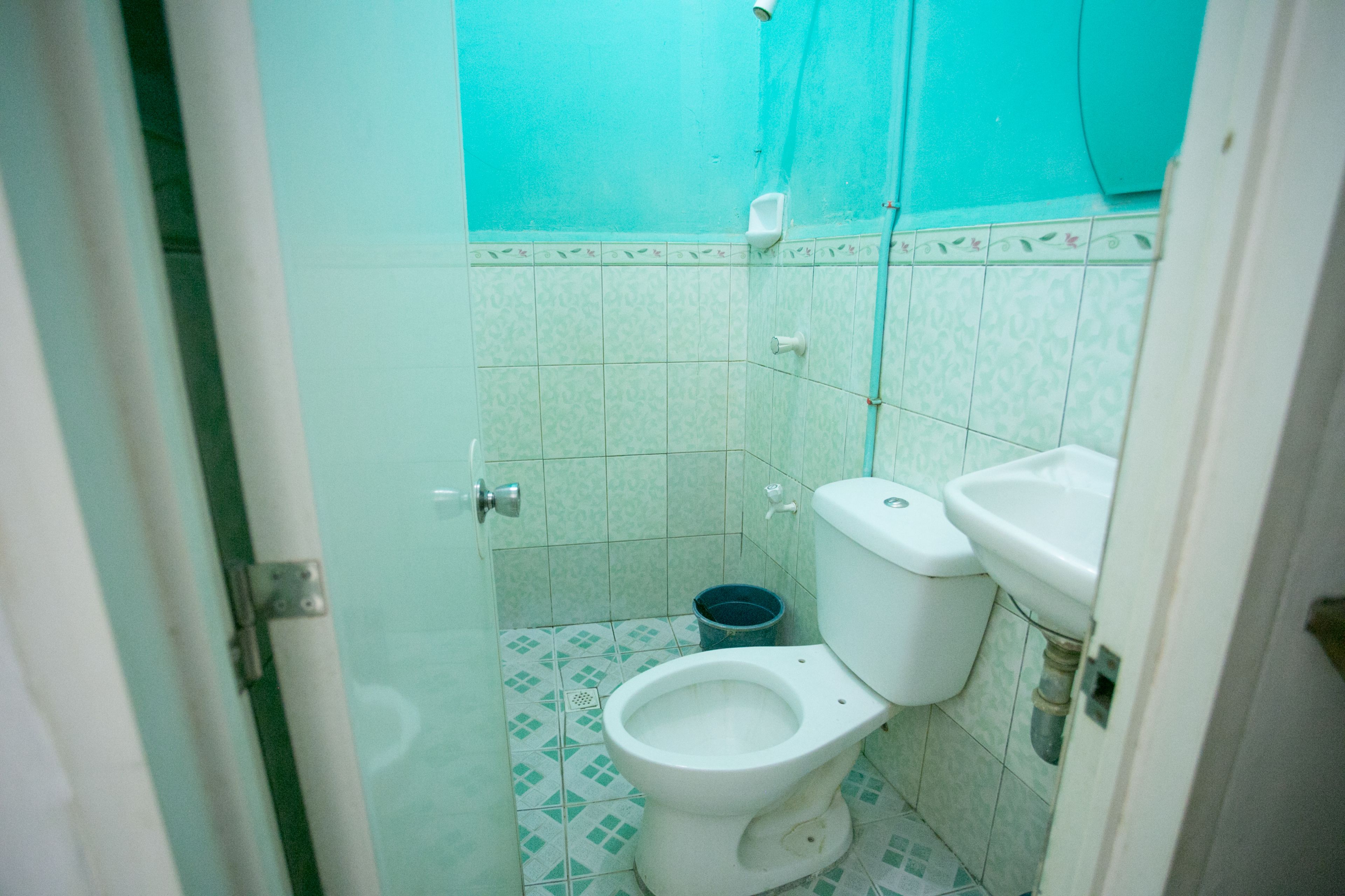 A small bathroom with a toilet, sink, and a blue bucket on the floor.