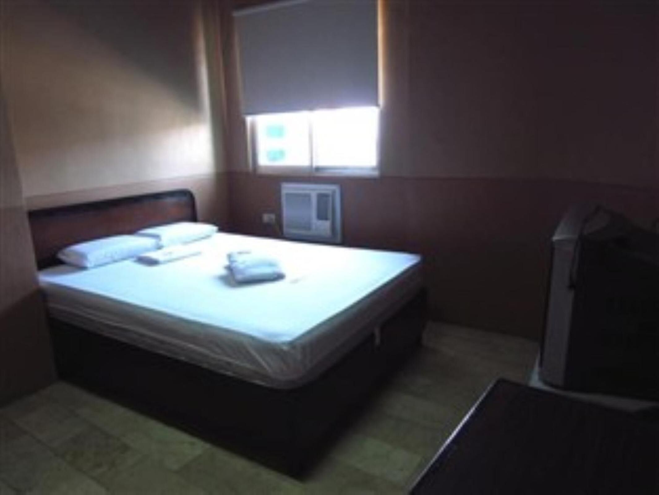 A small, dimly lit hotel room with a single bed, a small table, and a television.