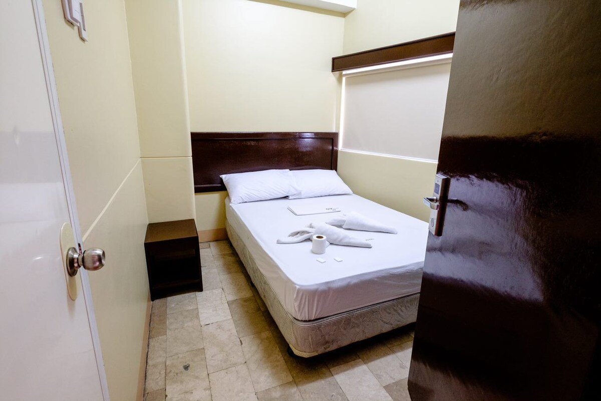 A small, neatly arranged bedroom with a single bed, a wooden headboard, and a white door.
