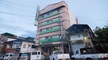 A multi-story building with a sign for GV Hotel. There are several parked vehicles in front, including a white pickup truck.