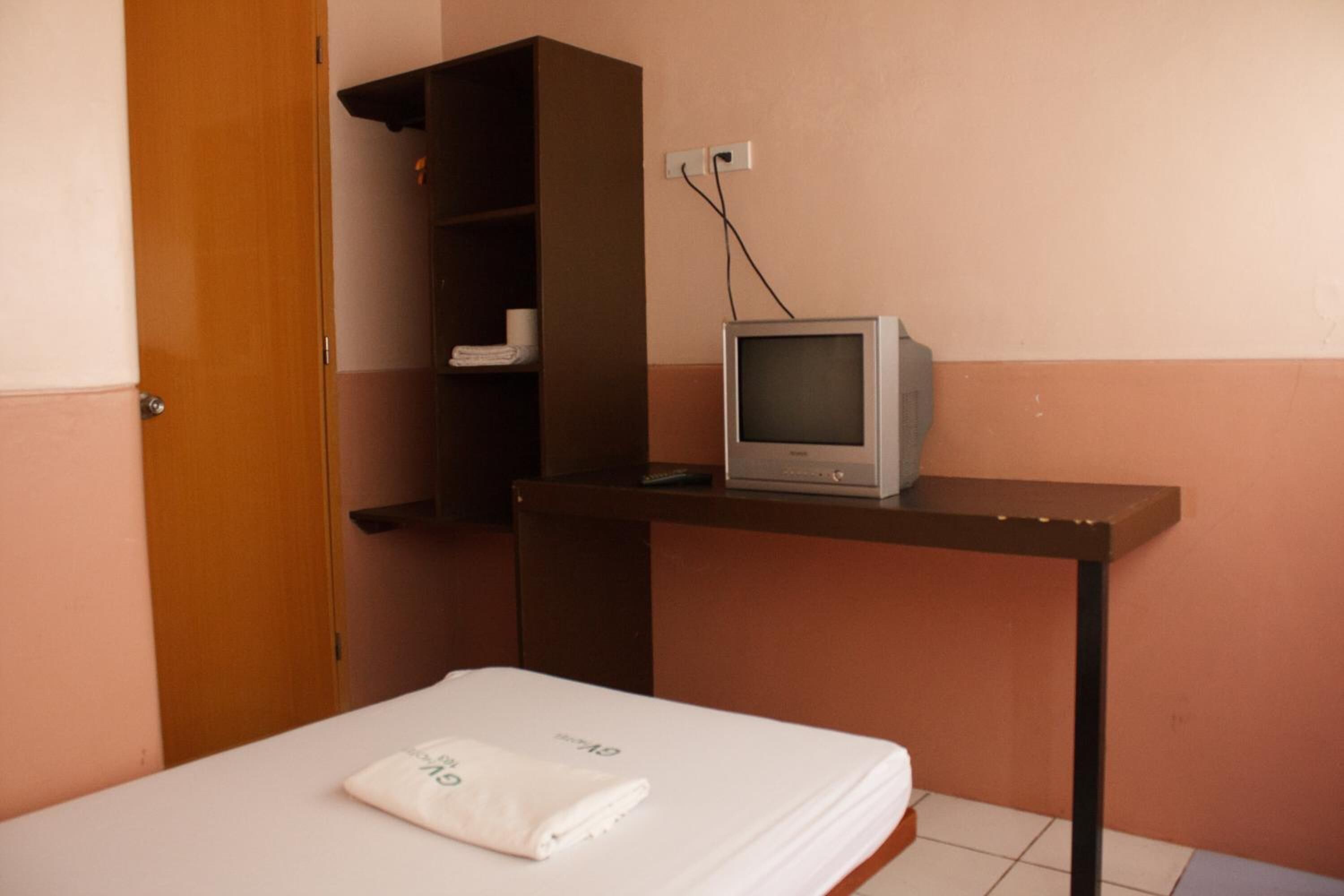 A hotel room with a bed, a small desk with a television, and a wardrobe.