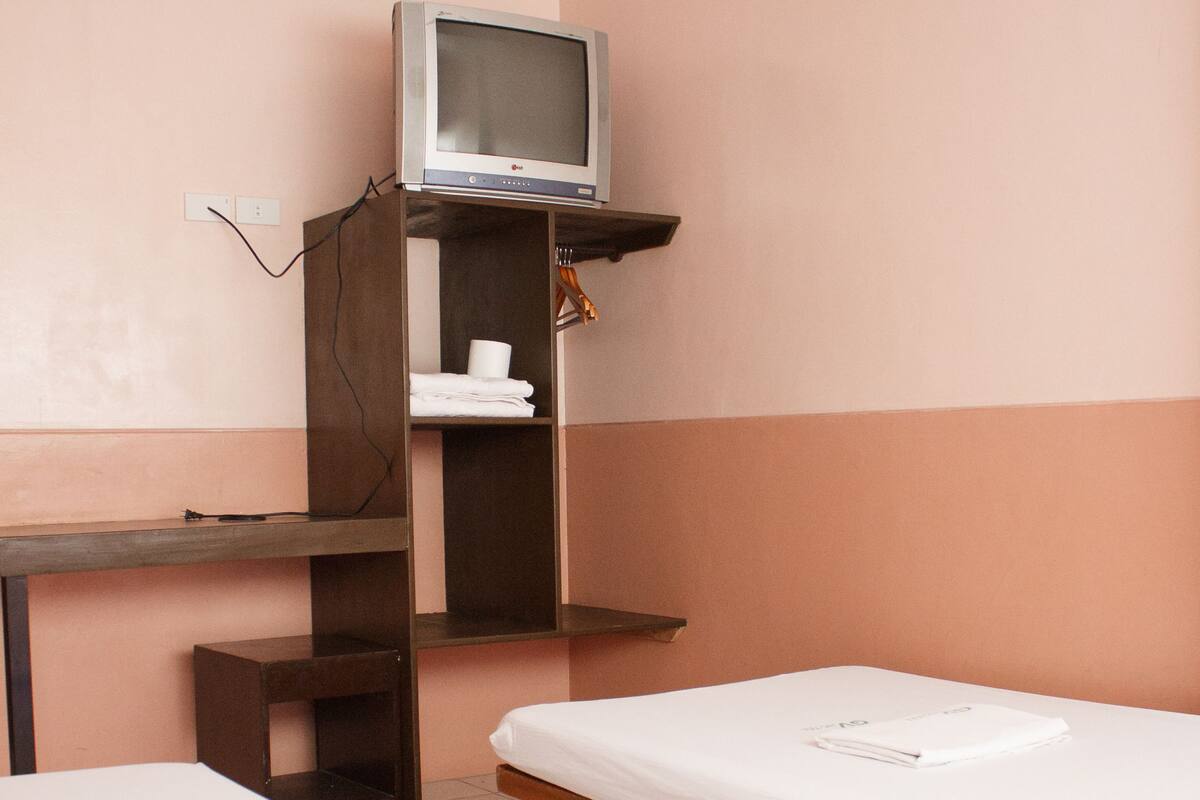 A small, single-room hotel room with a bed, a TV on a shelf, and a small table.