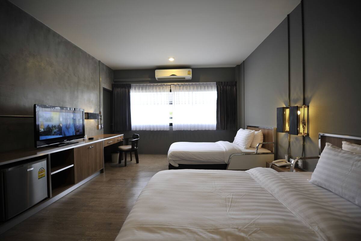 A hotel room with a TV, two beds, a desk, and a window with curtains.