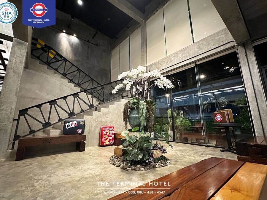 A modern hotel lobby with a staircase, a large potted plant, and a wooden bench.