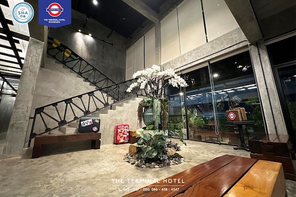 Un moderno vestíbulo de hotel con una escalera, una planta grande en maceta y un banco de madera.
