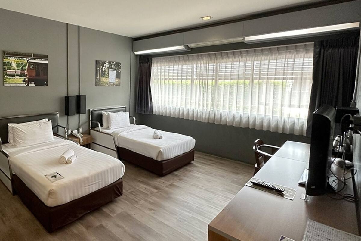 A hotel room with two beds, a desk, a chair, a TV, and a staircase.
