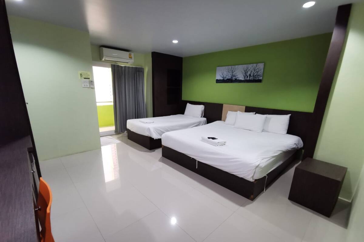 A hotel room with two beds, a green wall, and a window with curtains.