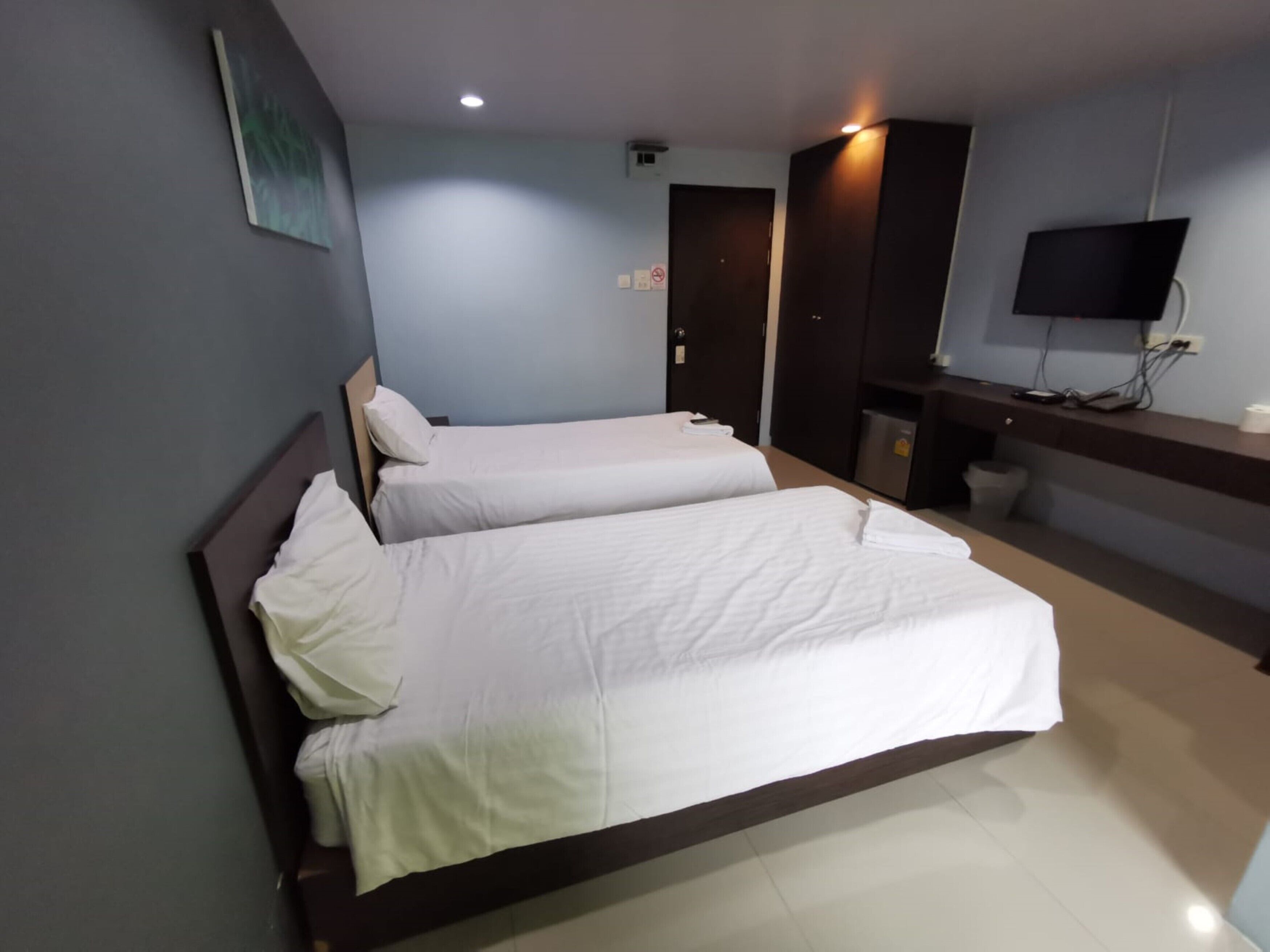 A hotel room with two single beds, a desk with a flat-screen TV, and a small trash bin.