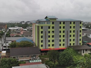 A multi-story building with a green and red facade, surrounded by other residential buildings and greenery. - The Peak Songkhla (Songkhla)