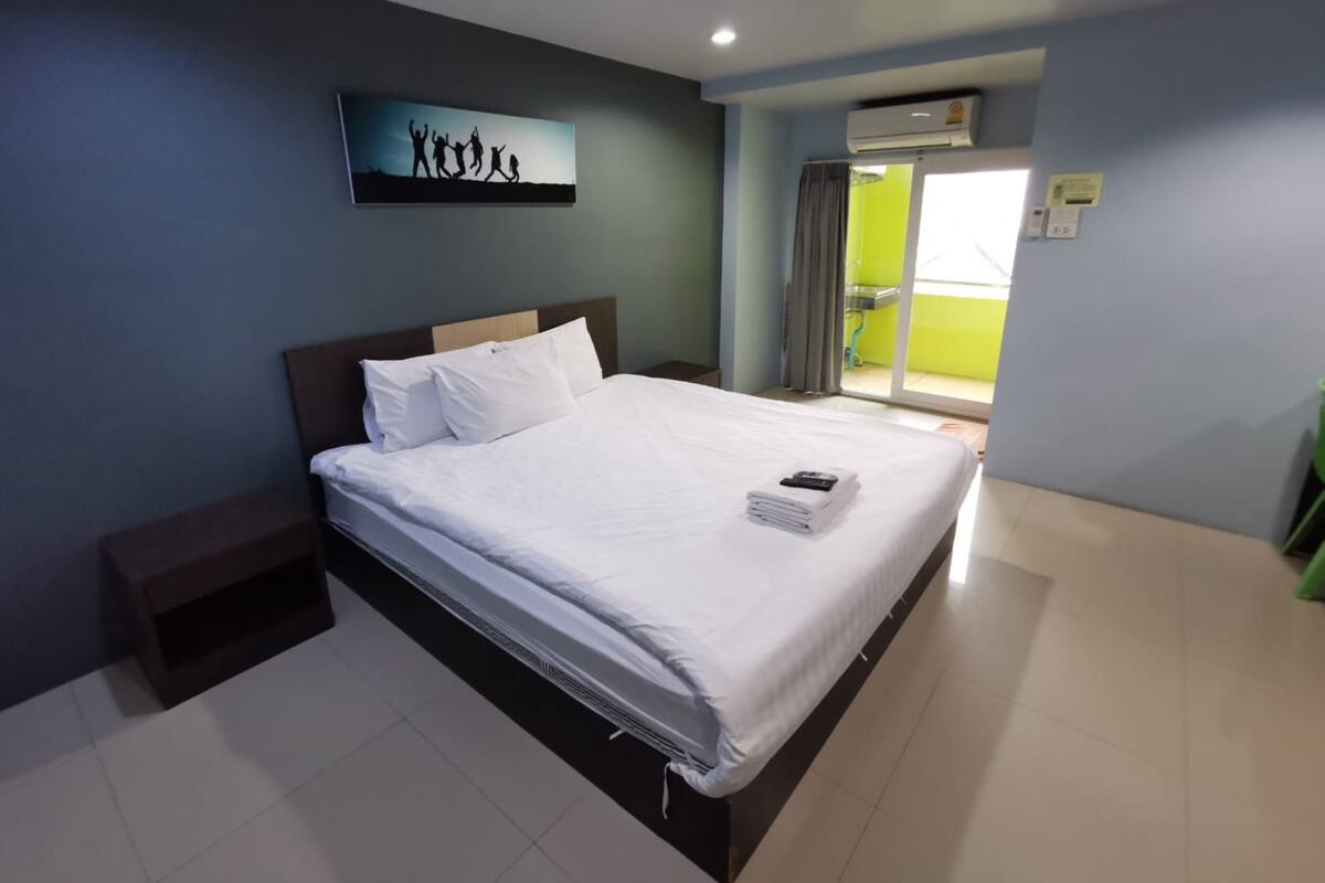 A neatly made bed with white linens in a hotel room with a view of a balcony.