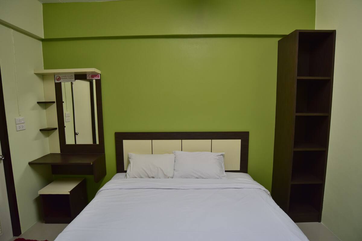 Un dormitorio con cama, mesita de noche, espejo y estante.