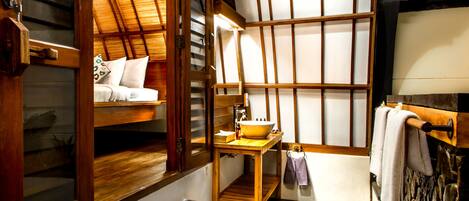 A traditional Japanese-style room with tatami flooring, a wooden table with a bowl, a bed with white bedding, and a stone wall.