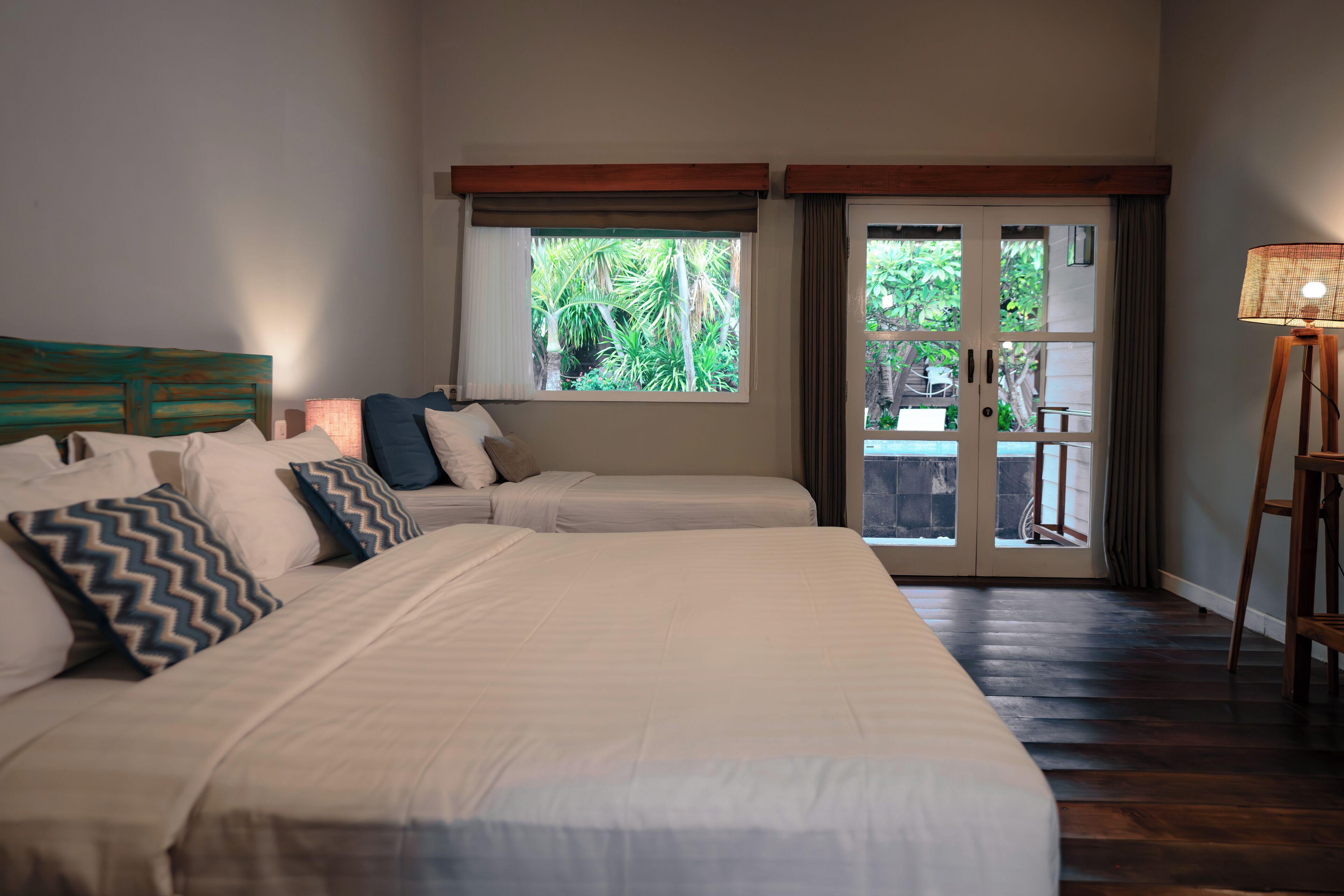 A bedroom with a large bed, a window with a view of greenery, and a door leading to an outdoor area.