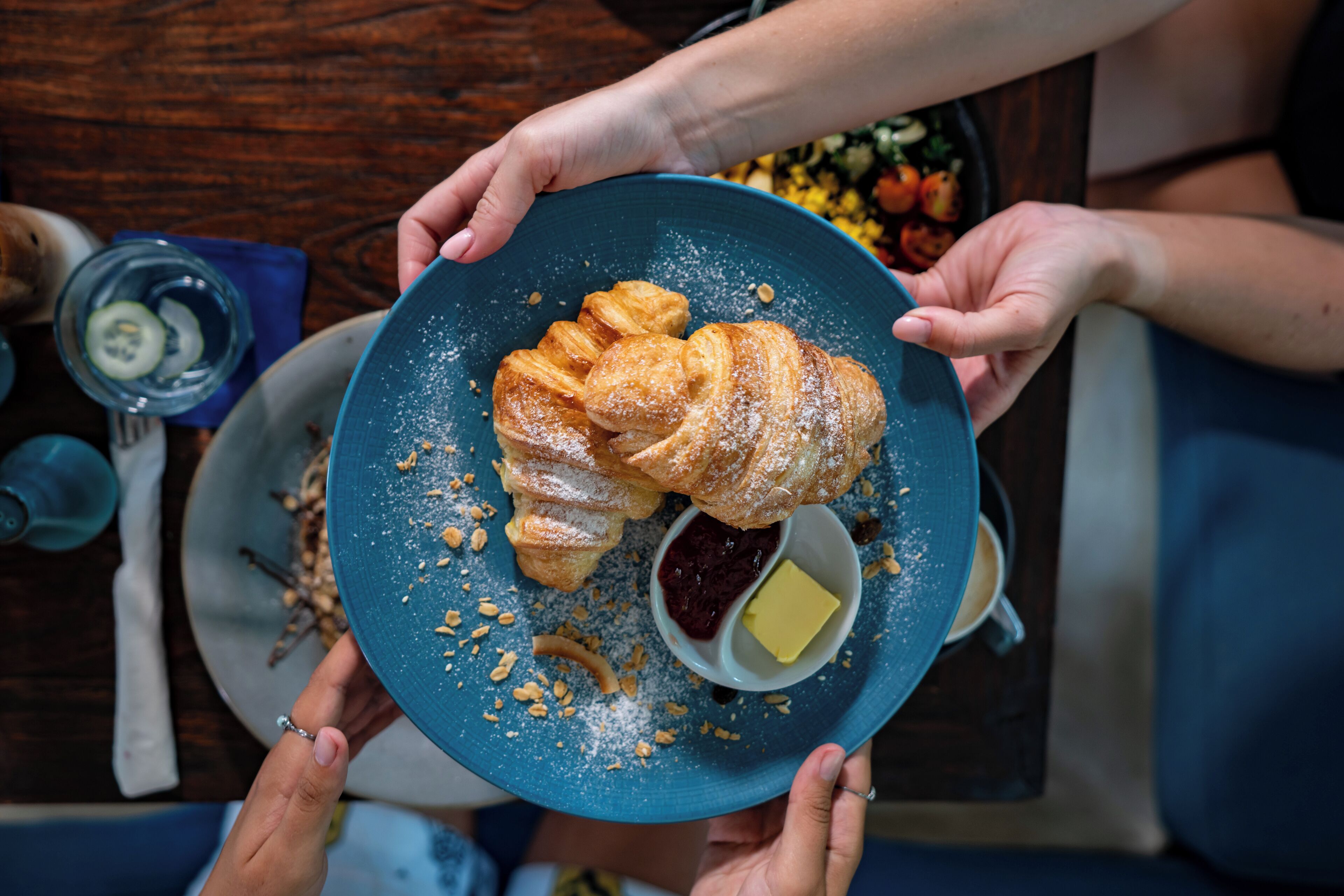 Una persona sosteniendo un plato azul con un croissant y un recipiente pequeño de mantequilla.
