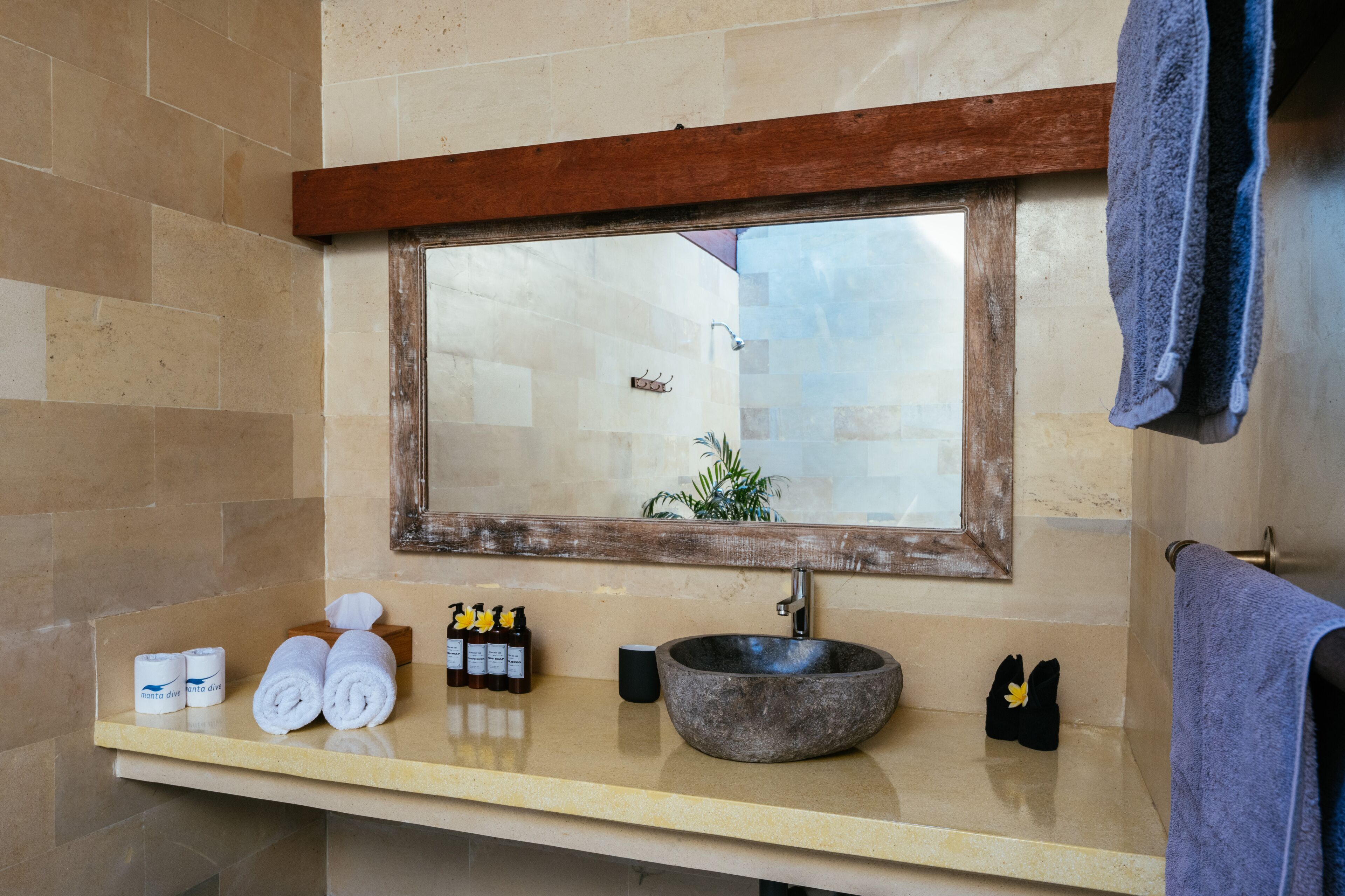 Casa de banho com lavatório de pedra, espelho com moldura de madeira e produtos de higiene no balcão.