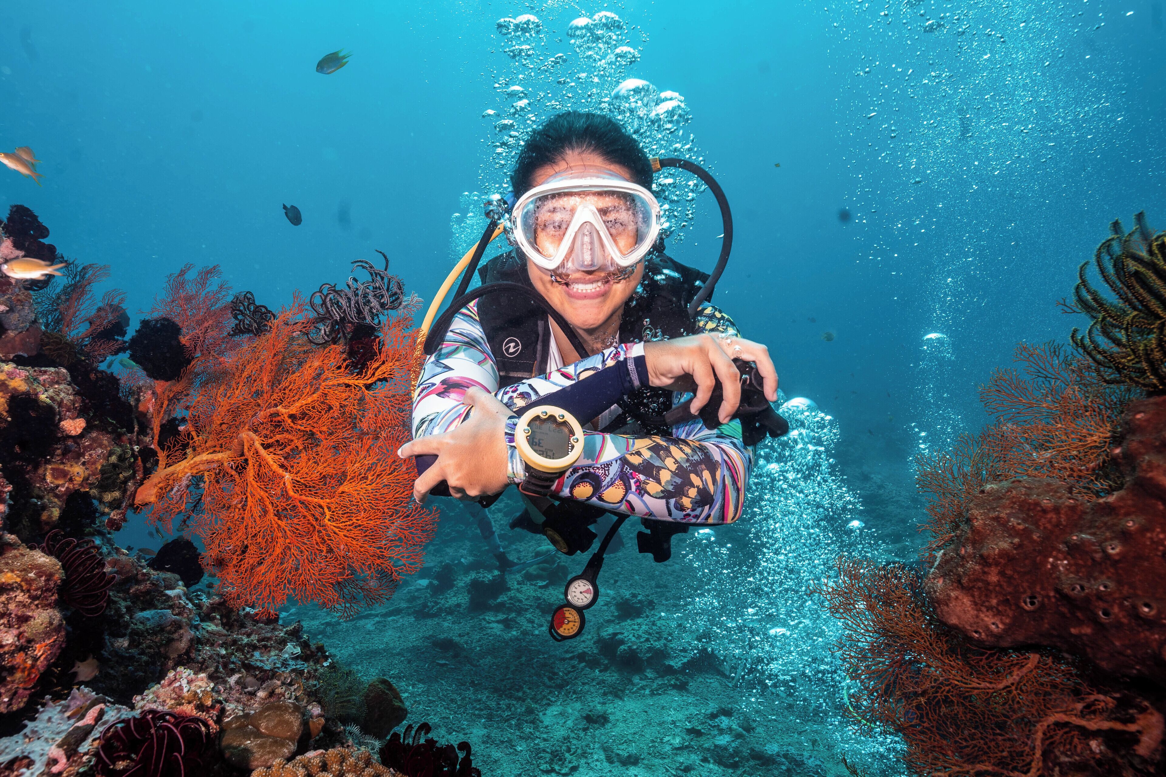Un buceador bajo el agua, rodeado de coral y peces.