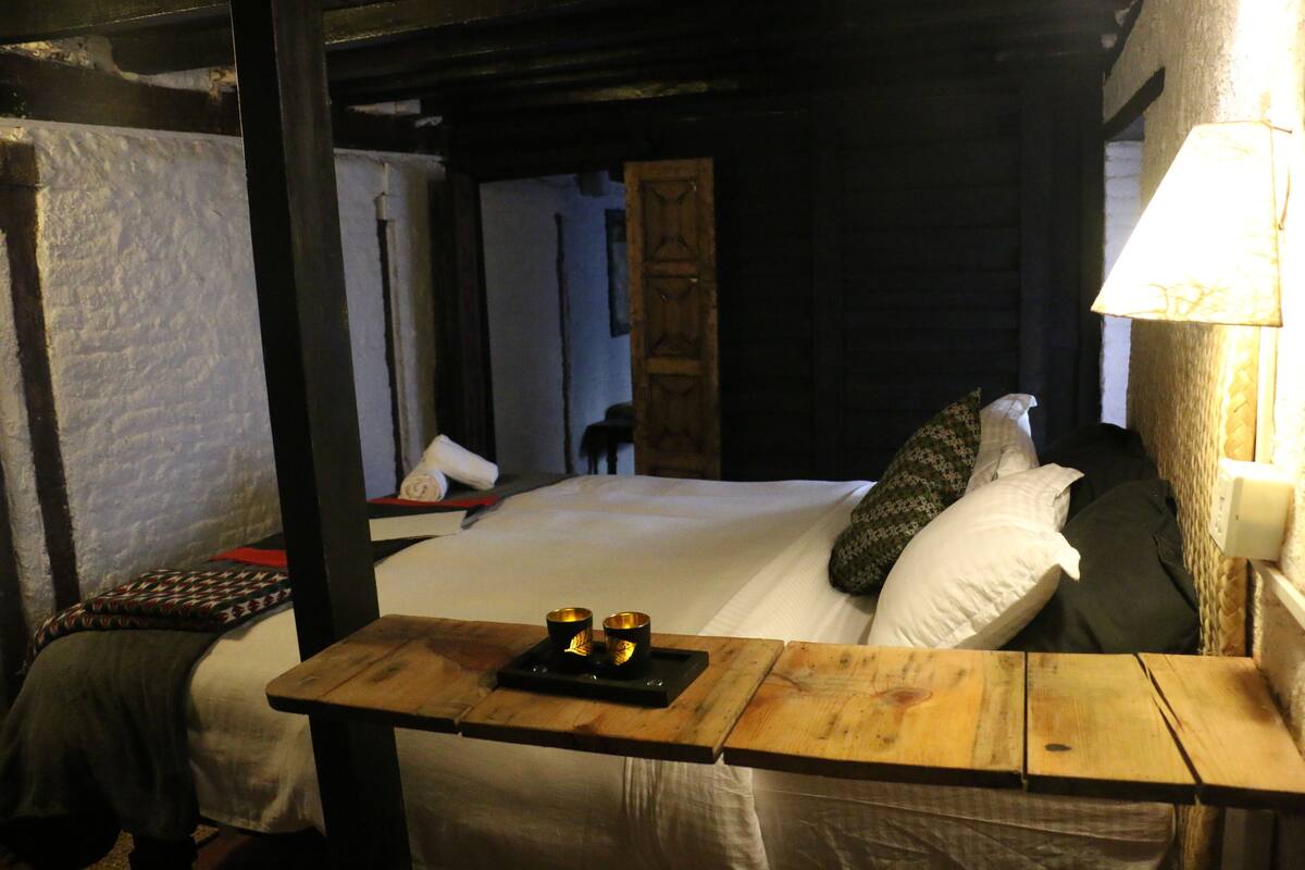A cozy room with a wooden bed, a nightstand with candles, and a view of a hallway.
