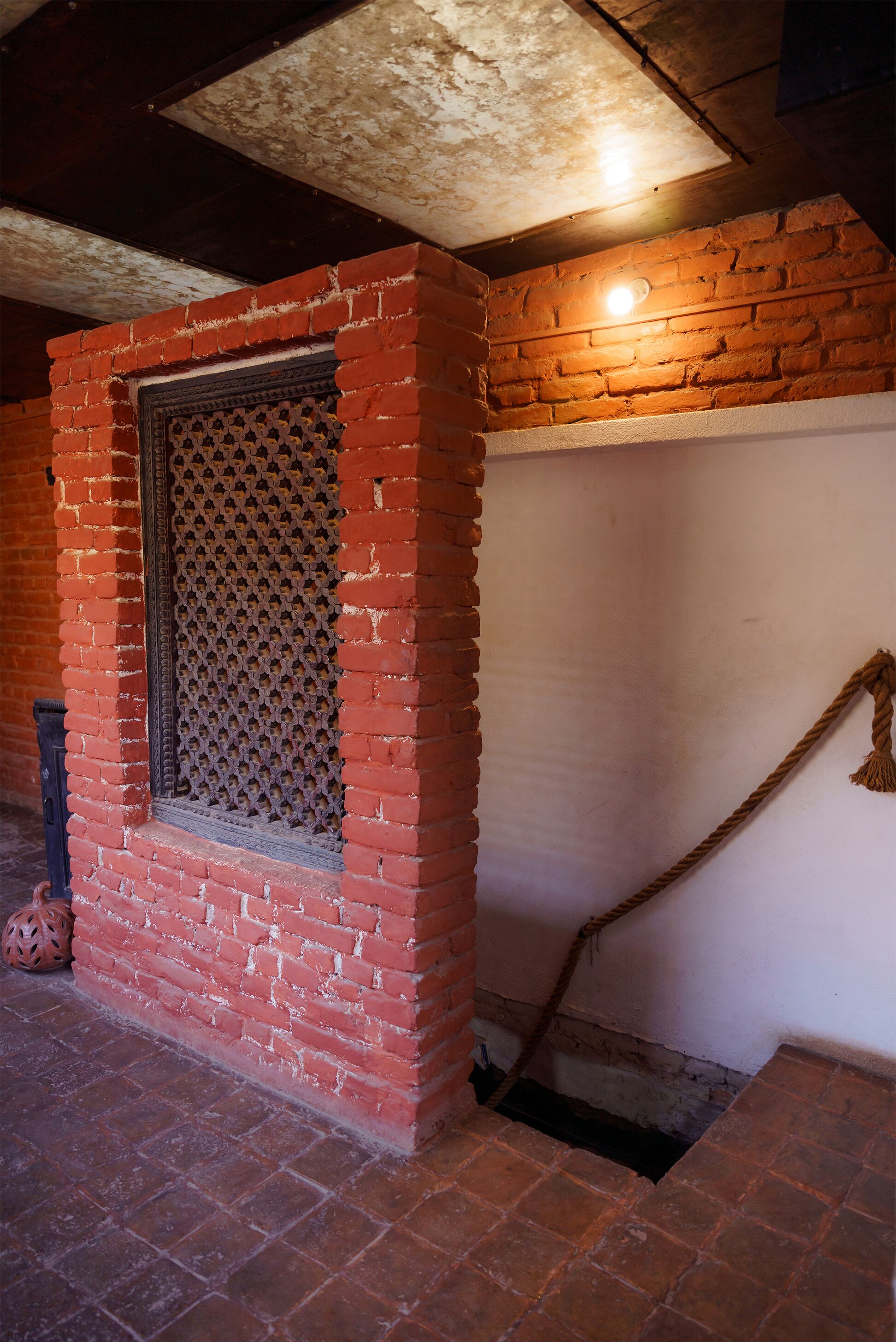 A brick wall with a window, a rope, and a small opening in the floor.