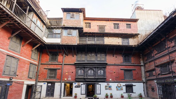 A courtyard with a table and chairs, surrounded by buildings with multiple stories and balconies. - Hira Guest House (Lalitpur)