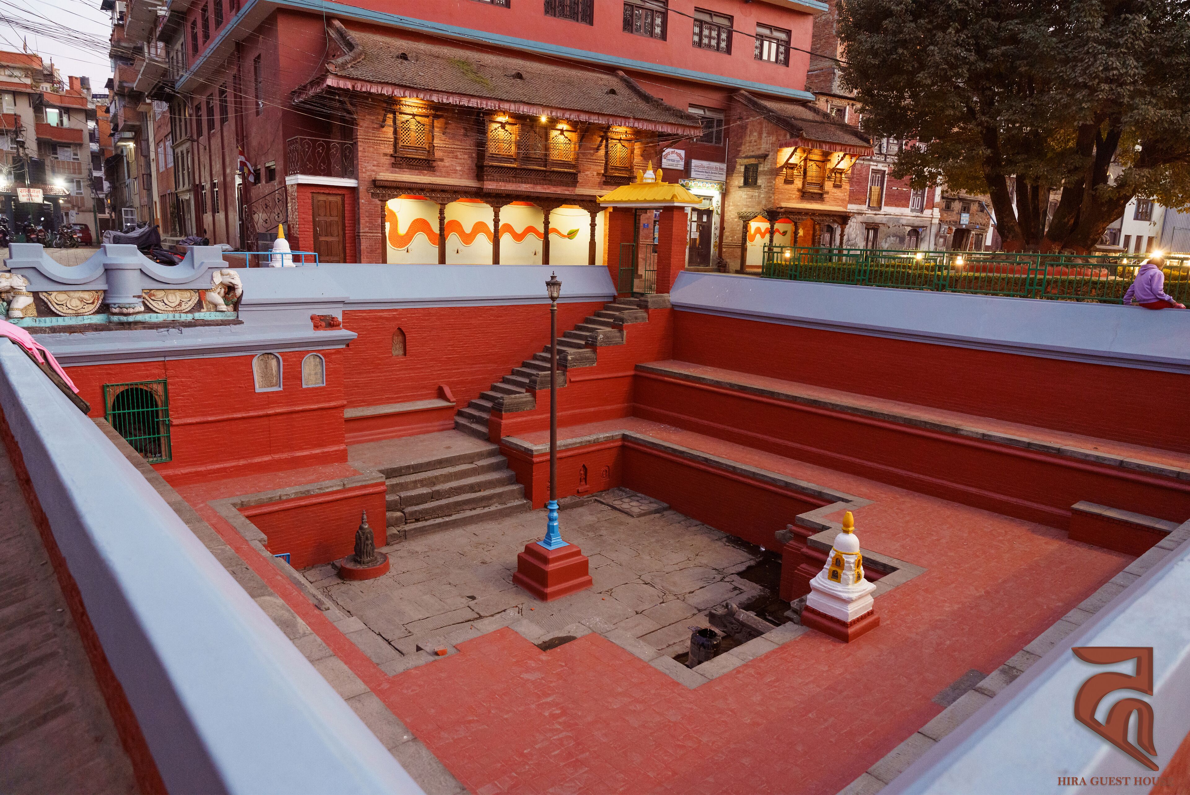 A courtyard with a staircase leading to a building with traditional architecture, a small shrine, and a green fence.