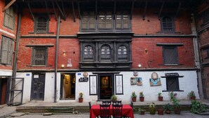 A traditional building with a red brick facade, multiple windows, and a small outdoor seating area with a red tablecloth. - Hira Guest House (Lalitpur)