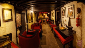 A dimly lit corridor with red upholstered seating and framed artwork on the walls. - Hira Guest House (Lalitpur)
