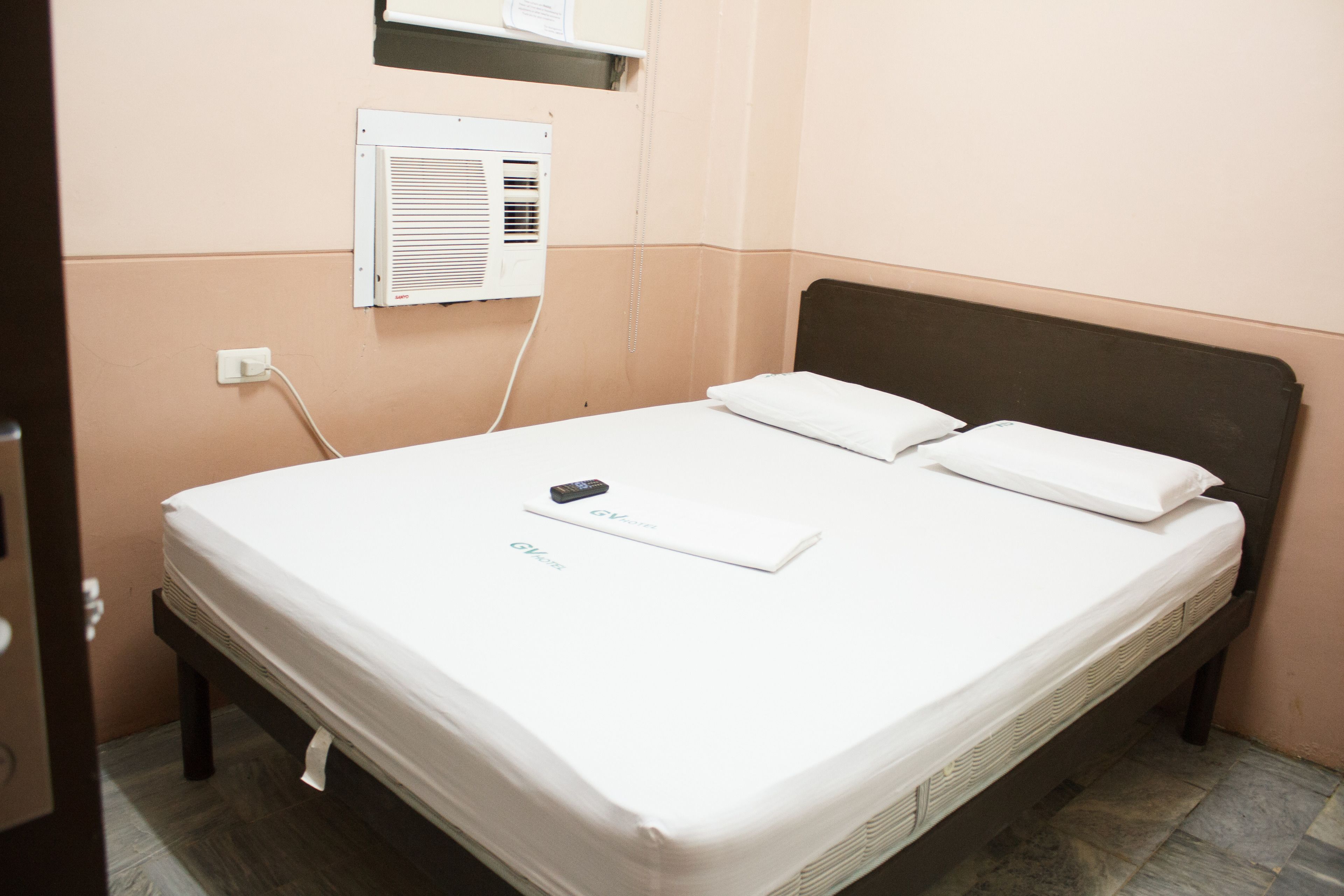 A single bed with white bedding, a remote control, and a pillow on a dark headboard.