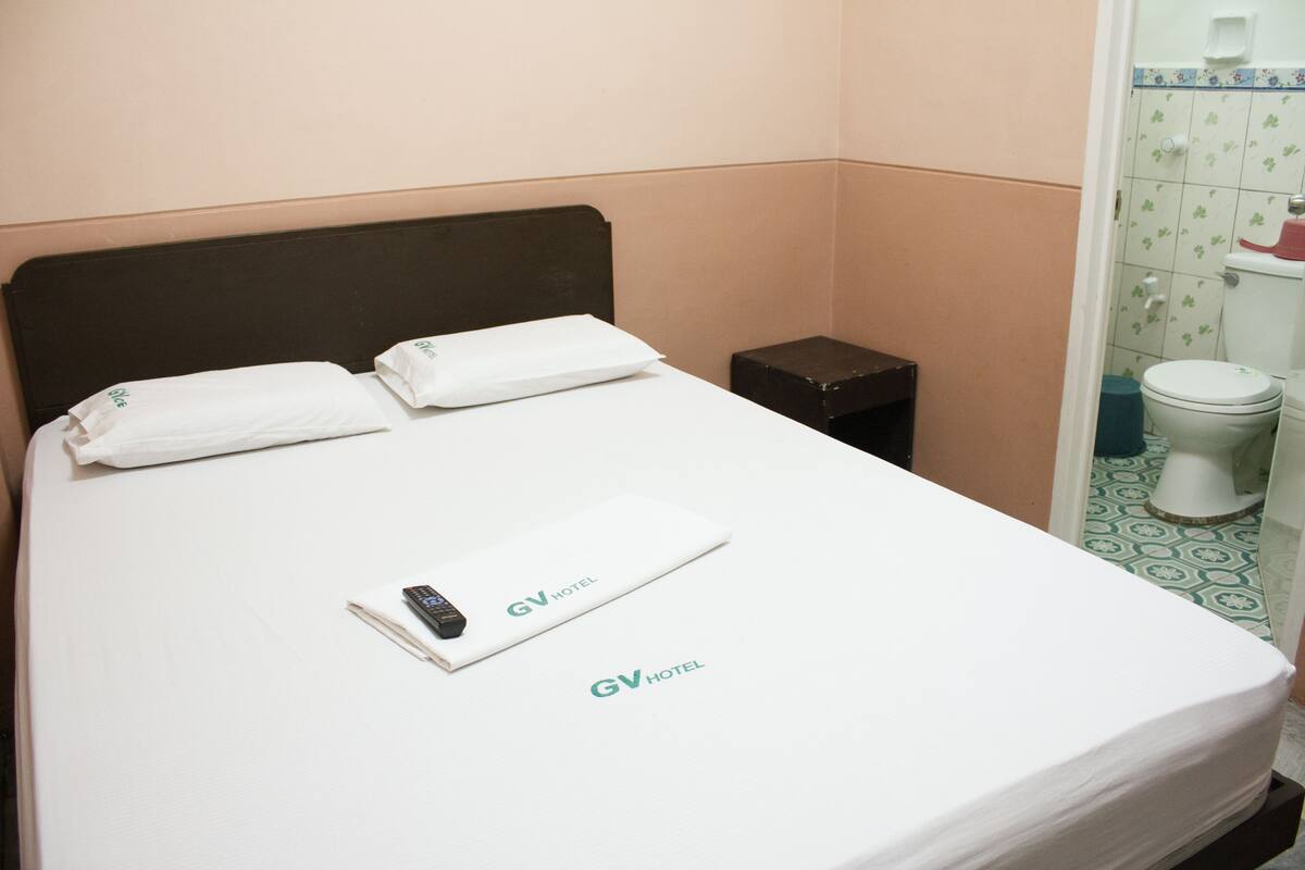 Une chambre d’hôtel avec un lit, une table de chevet et une petite poubelle noire.