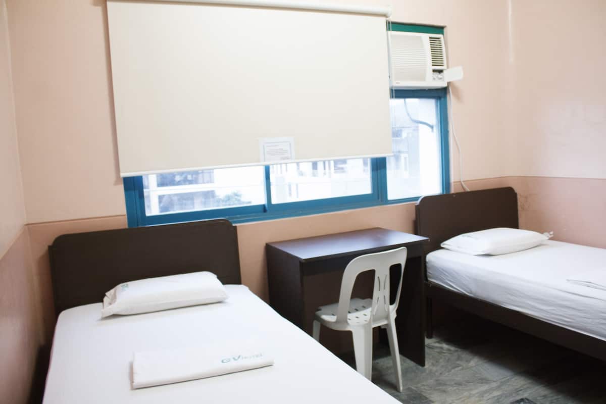 Une chambre d’hôtel avec deux lits simples, un bureau, une chaise et un climatiseur fixé au mur.