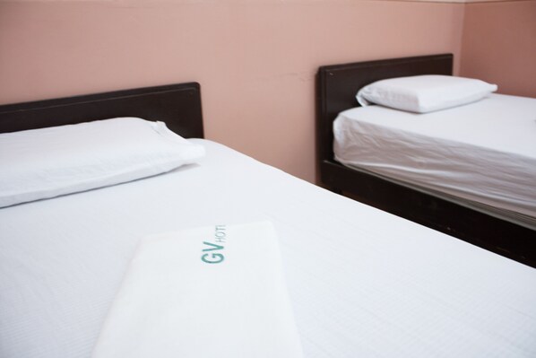 Una habitación de hotel con dos camas individuales, cada una con colchón y almohada blancos.