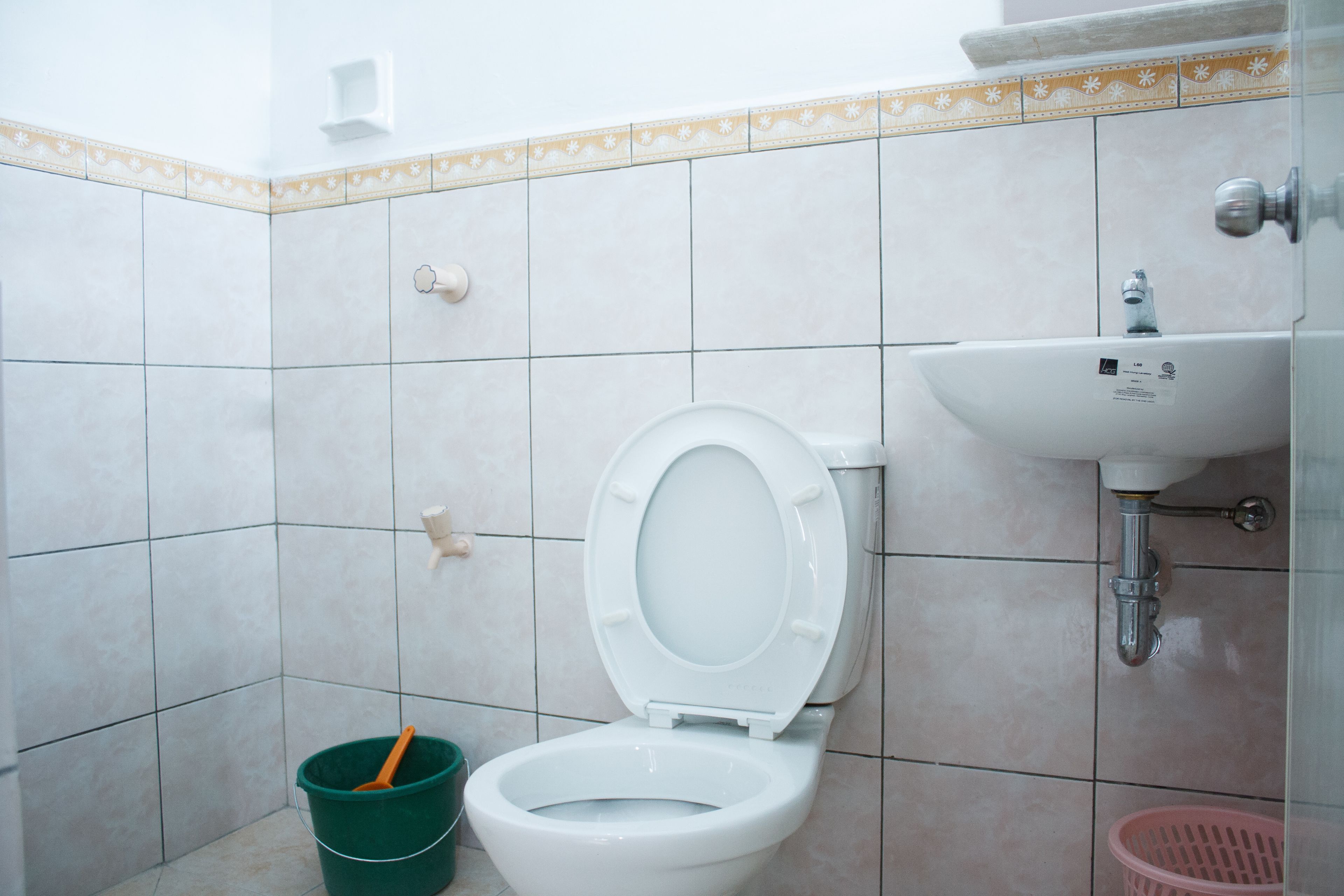 A bathroom with a toilet, a sink, and a green bucket.