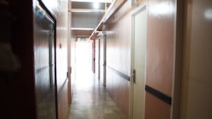Un pasillo con puertas a ambos lados, piso de baldosas y un letrero de salida al fondo.