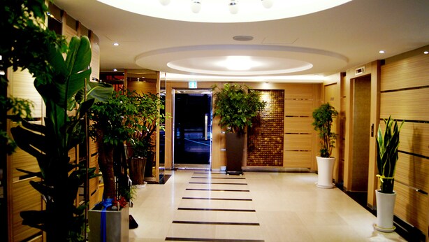 A hotel lobby with a modern design, featuring a central staircase, potted plants, and a wooden wall. - Princess Hotel (Seoul)