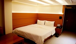 A hotel room with a wooden headboard, a bed with white bedding, a bedside table with a phone, and a small trash bin. - Princess Hotel (Seoul)
