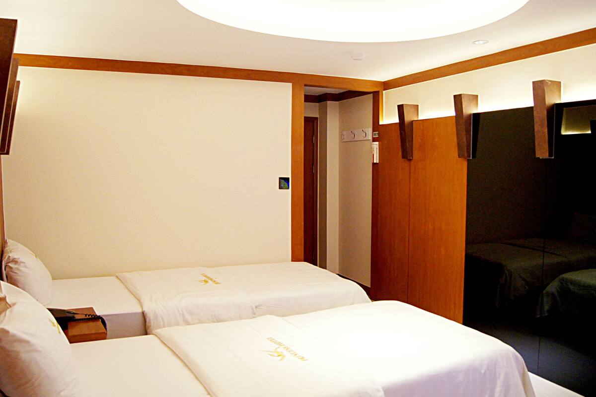 A hotel room with two beds, a wooden wardrobe, and a small desk.