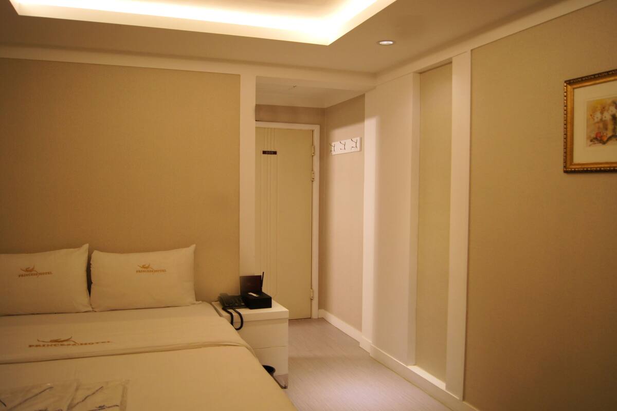 A hotel room with a bed, bedside table, and a painting on the wall.