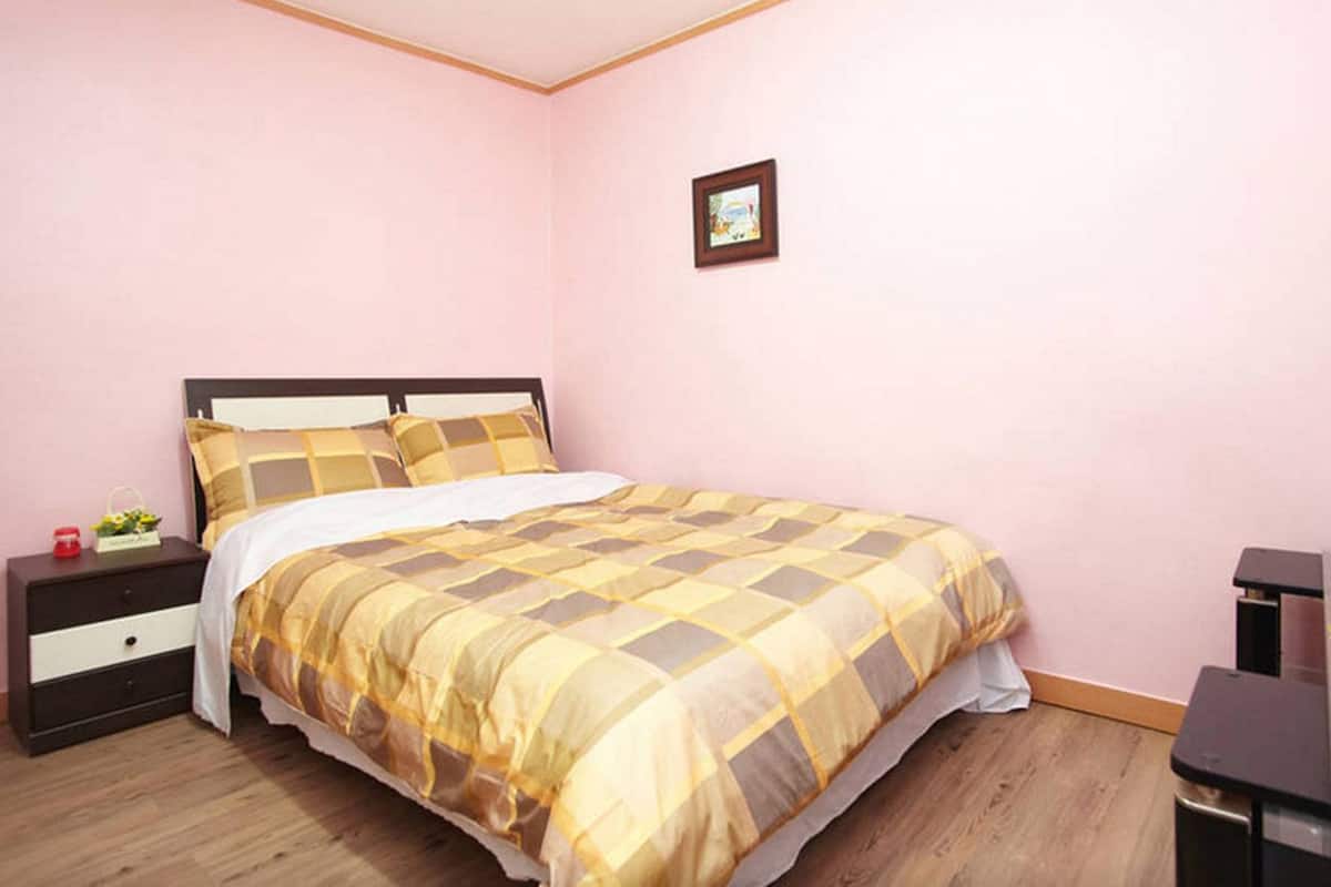 A bedroom with a bed, a nightstand, a dresser, and a TV.