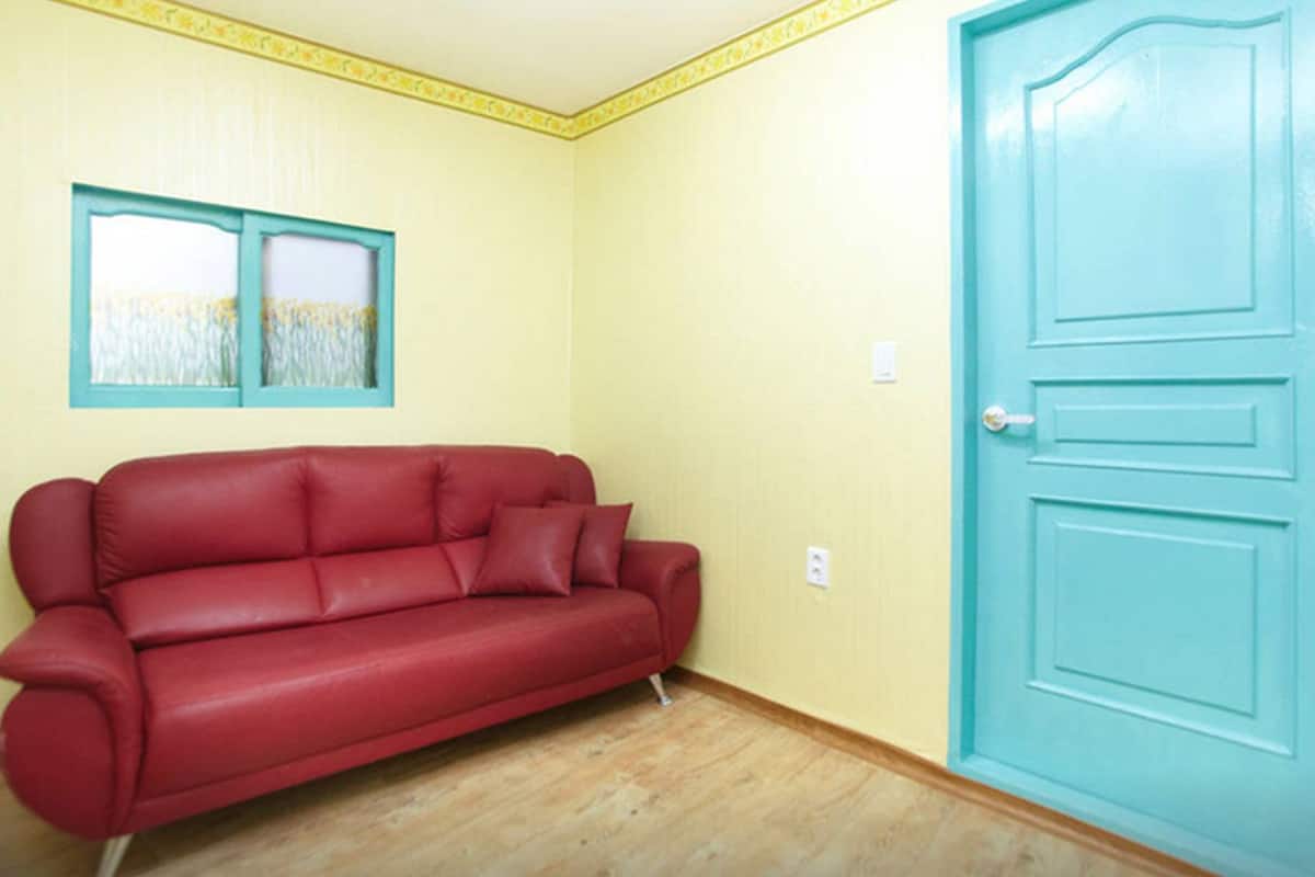 A room with a red sofa, a blue door, and a window with a view of a field.