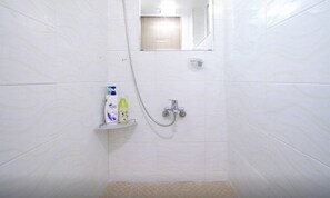 A bathroom with white tiled walls, a shower with a handheld showerhead, and a small shelf with toiletries.