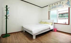 A bedroom with a single bed, a coat rack, a window with a view of a balcony, and a wall with a decorative mural.