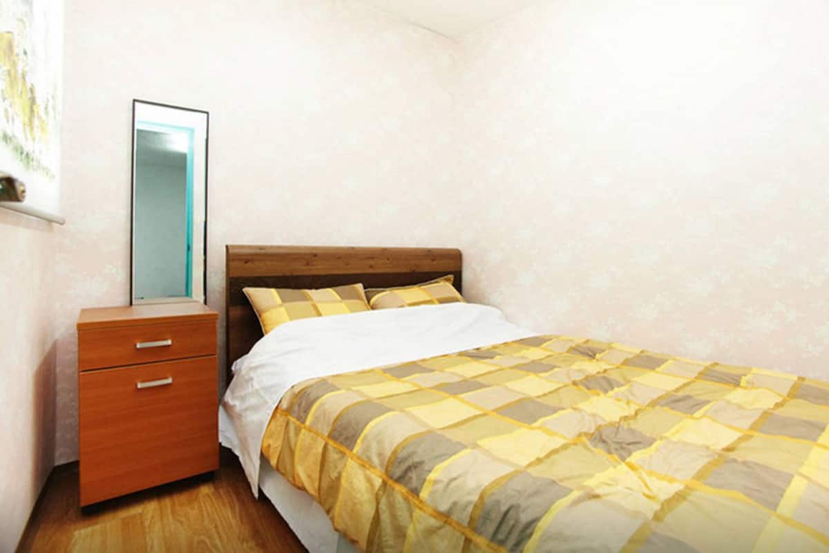 A bedroom with a bed, a wooden nightstand with drawers, and a mirror.