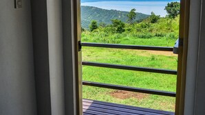 Une porte-fenêtre donnant sur un balcon d’où l’on peut admirer un paysage verdoyant et un plan d’eau.