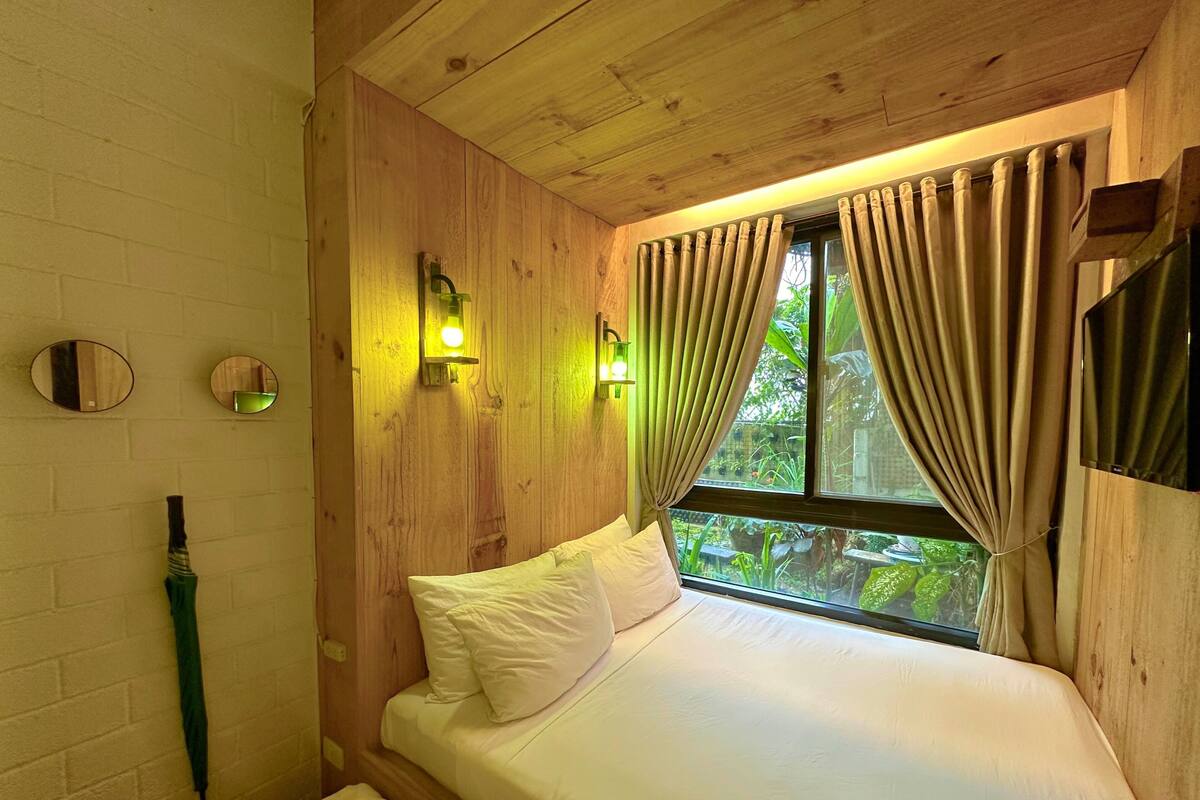 Een kamer met houten lambrisering, een bed, een spiegel en een raam met gordijnen.