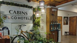 Un hall d’hôtel avec une enseigne indiquant « CABANES D’ÉCOHÔTELS », un vélo, des plantes en pot et une étagère avec des bouteilles.
