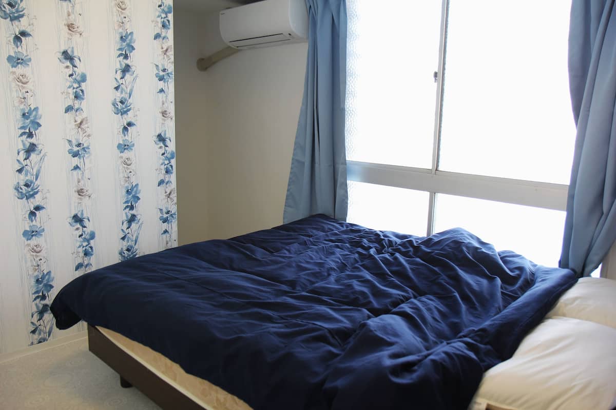 A bedroom with a bed, a window with curtains, and an air conditioning unit on the wall.