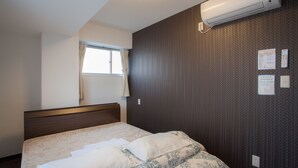 Habitación de hotel con cama, ventana con cortinas, equipo de aire acondicionado y pared con termostato y cartel.