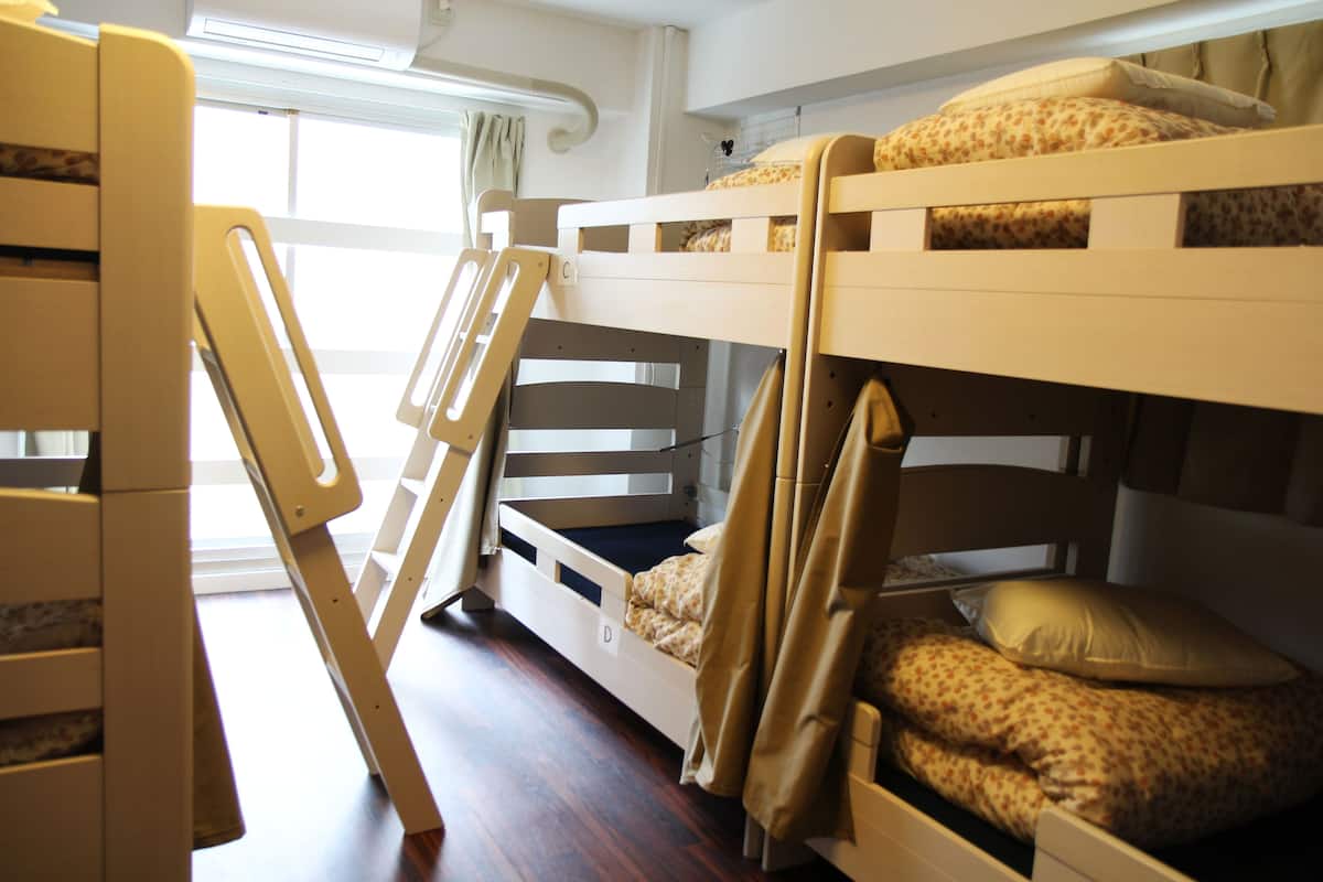 A bunk bed room with a ladder, a chair, and a window with curtains.