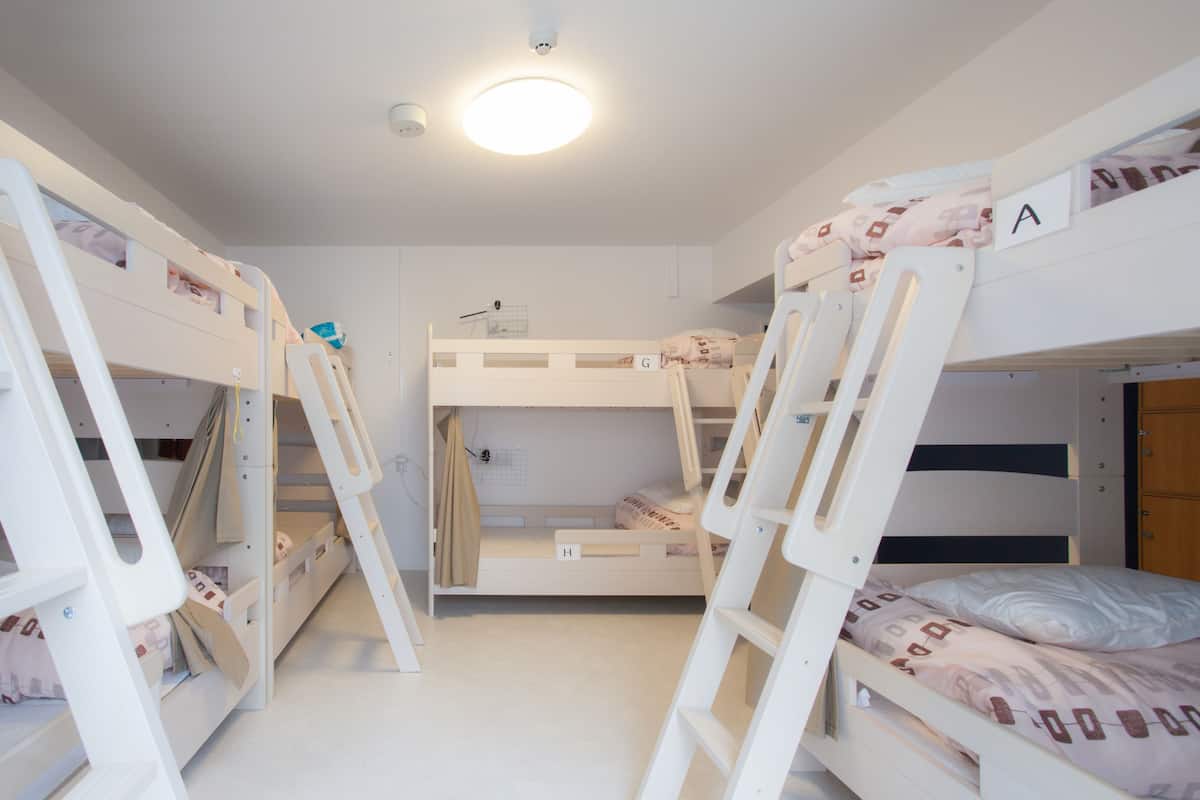 A bunk bed room with a bunk on the left and a lower bunk on the right. There is a ladder on the left side of the room.