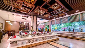 A modern hotel lobby with a buffet area, wooden ceiling design, and large windows offering a view of greenery. - Muong Thanh Xa La (Hanoi)