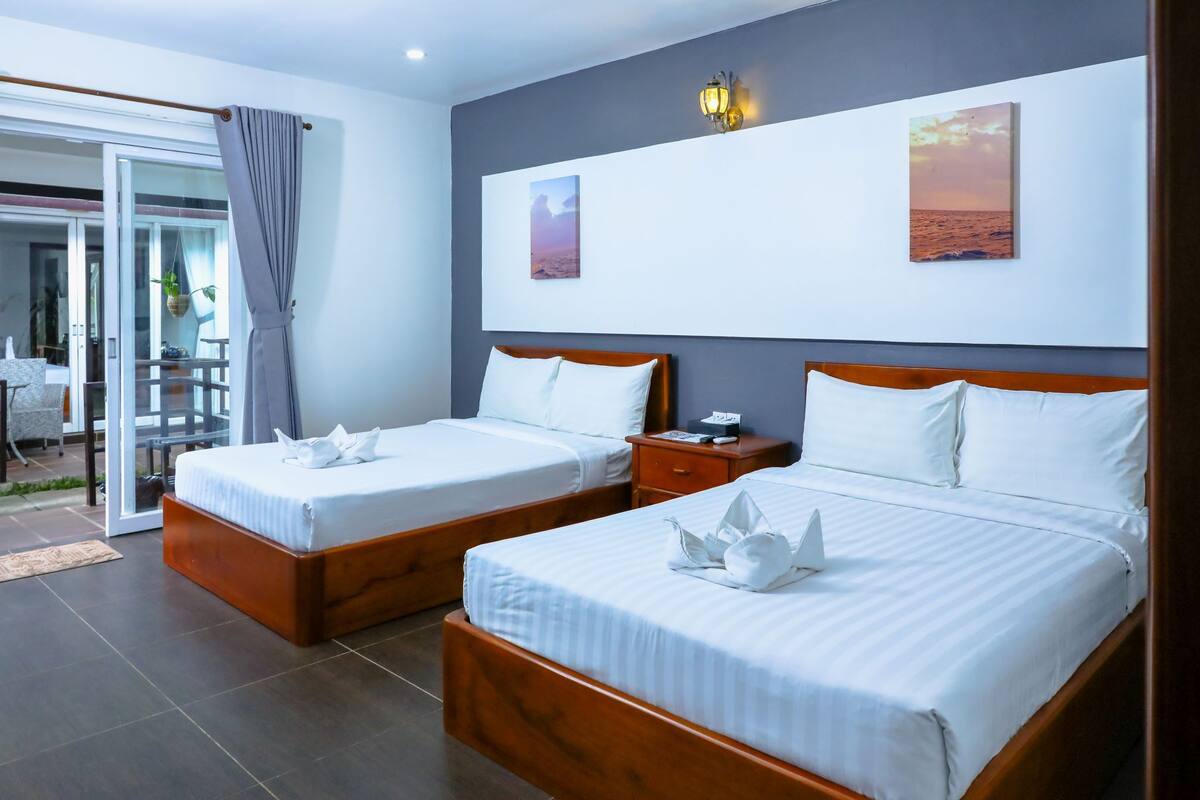 A hotel room with two beds, a sliding glass door to a balcony, and artwork on the walls.